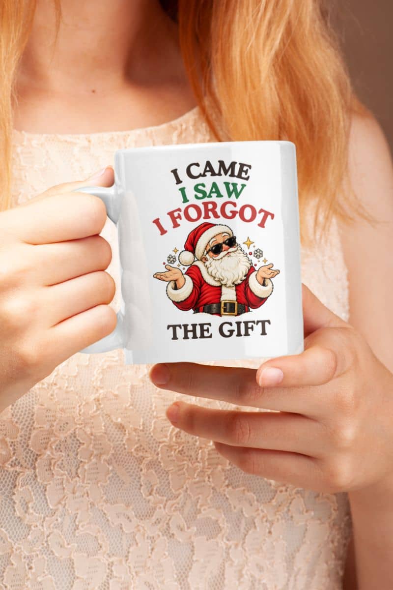 Woman in a cream lace top holding a Holiday coffee mug featuring a funny shrugging Santa and festive Christmas lettering.