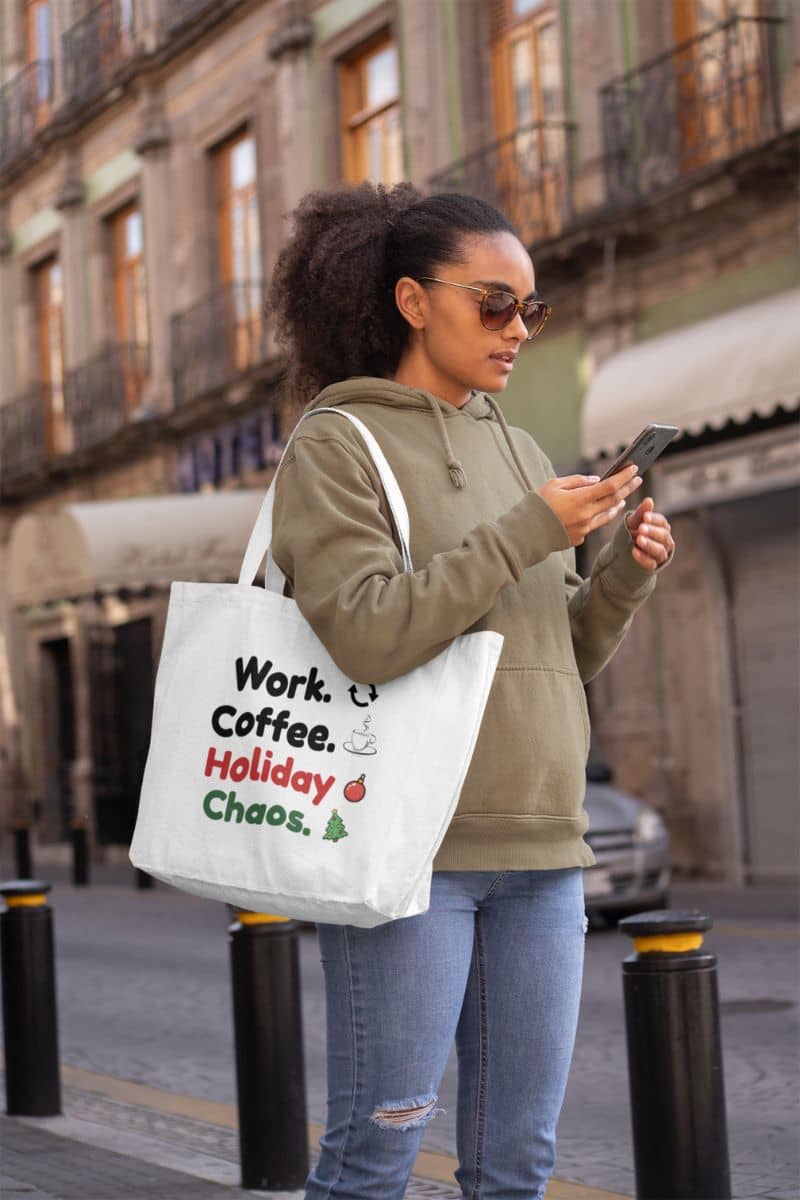 holiday errands tote with a woman walking on a city street holding a phone, wearing sunglasses and carrying a tote bag with text 'Work. Coffee. Holiday Chaos.'.