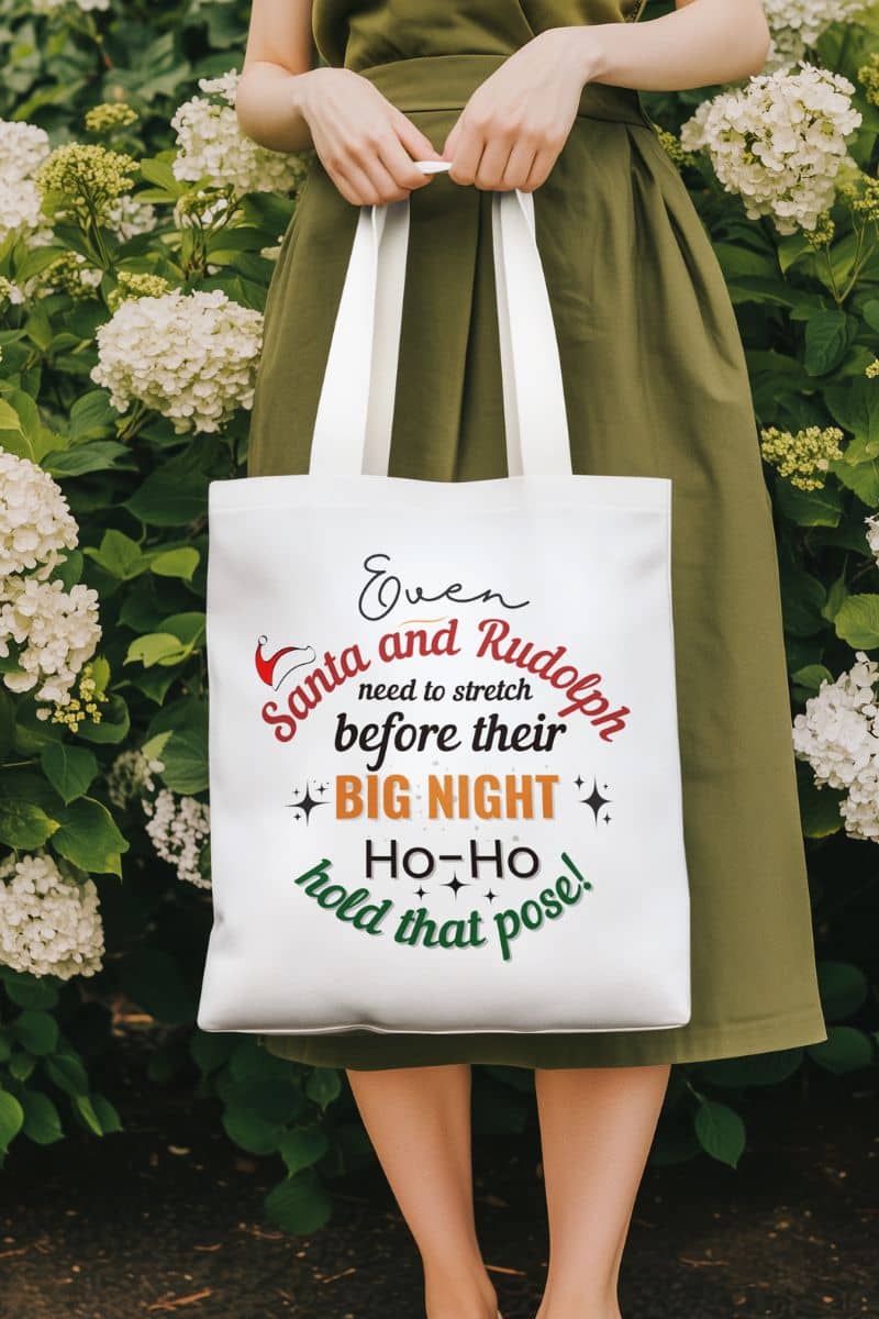 holiday gift bag for women with a person holding a tote bag with text 'Event Santa & Rudolph Need to Stretch Before their Big Night. Ho-Ho-Hold That Pose!', standing in front of the flower garden