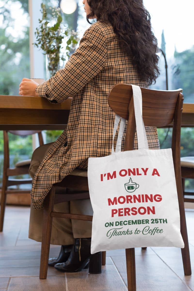 holiday gift haul tote with a person sitting at a table with a tote bag that reads 'I'm only a morning person on December 25th thanks to coffee'.