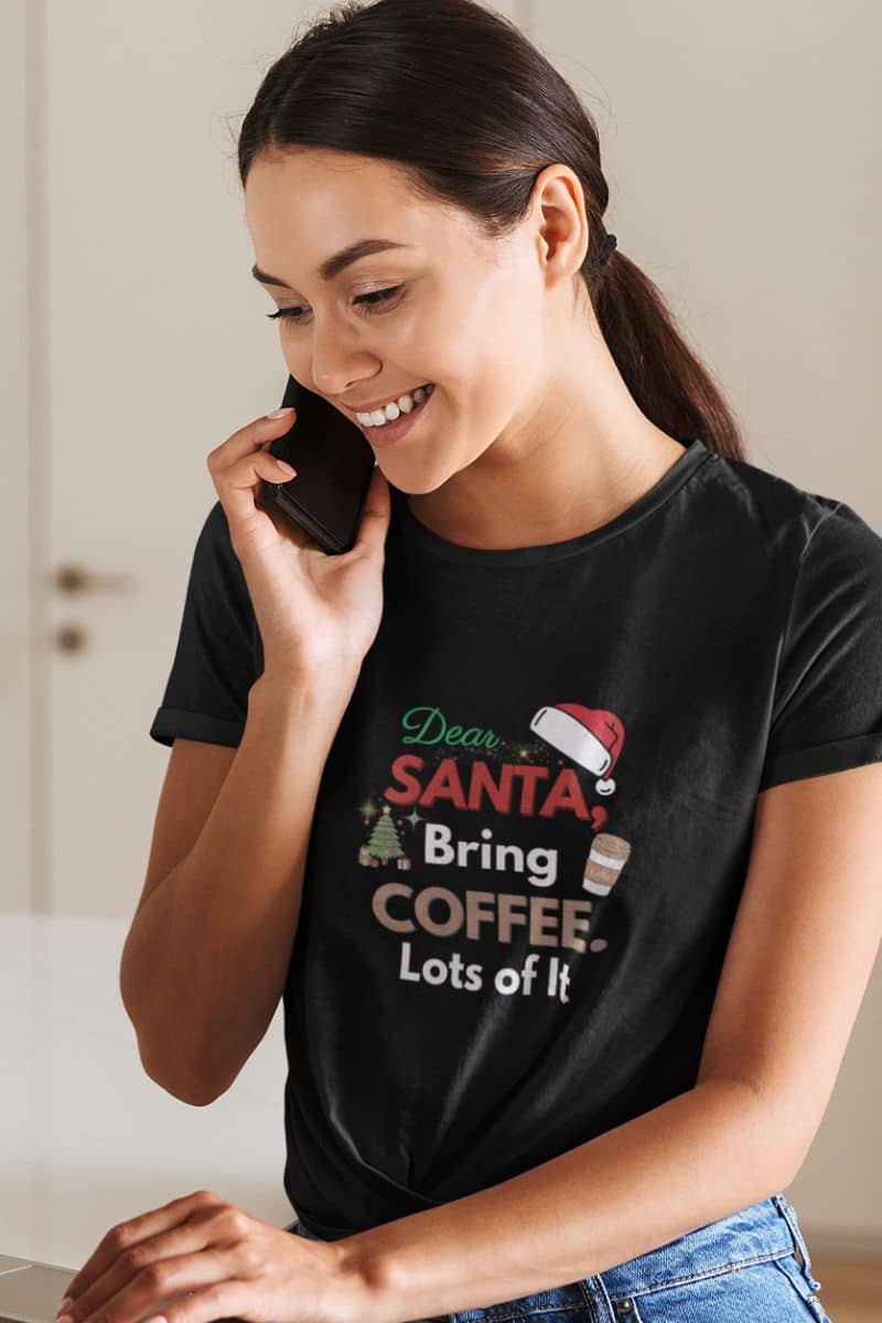 holiday humor tee with a woman wearing a black t-shirt with a Christmas-themed design, sitting at a desk.