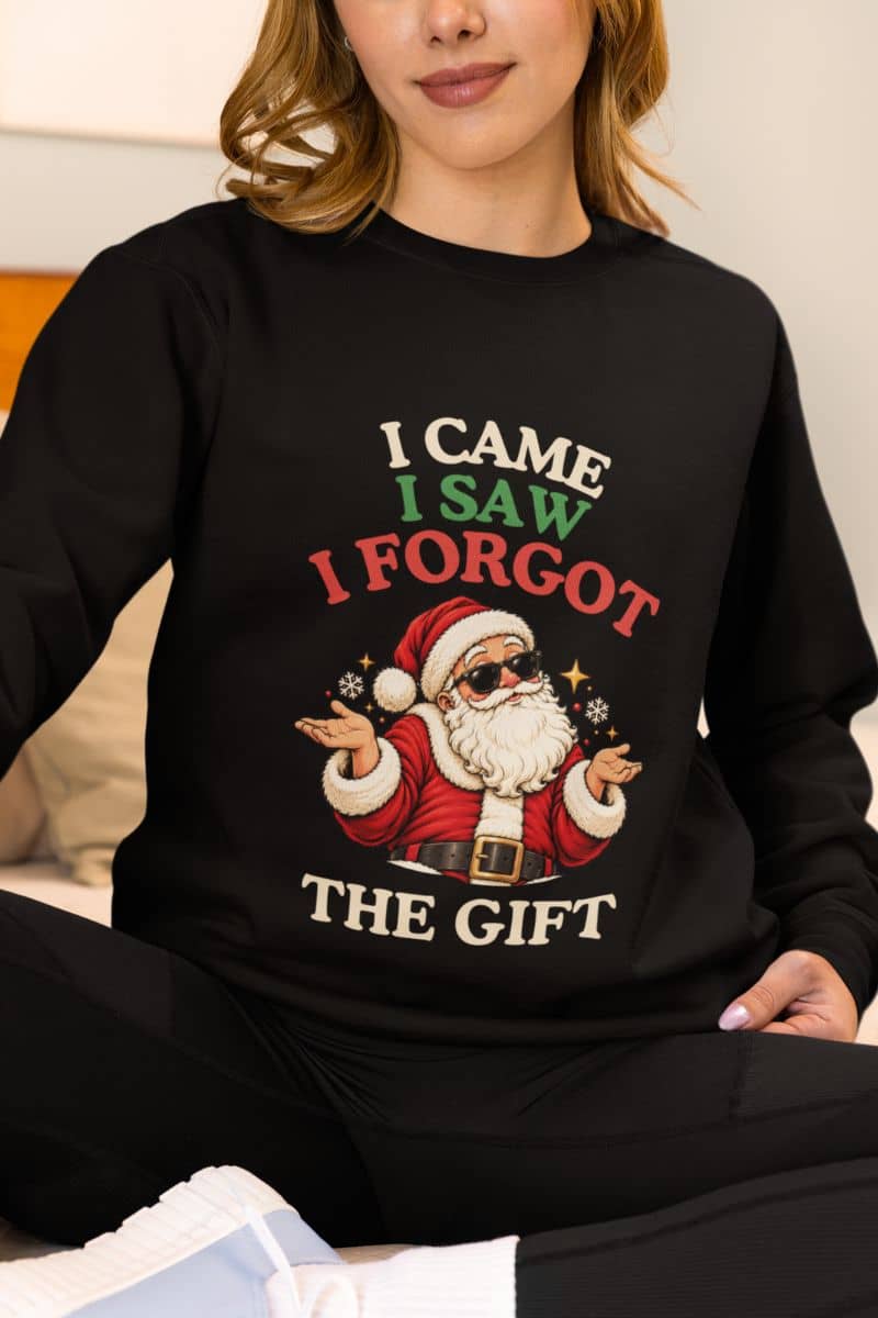 Woman sitting comfortably in a black holiday party sweatshirt featuring a sunglasses-wearing Santa and the funny “I Came. I Saw. I Forgot the Gift” quote.