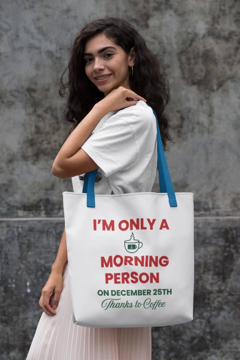 holiday shopping tote with a woman holding a tote bag with text 'I’m Only a Morning Person on December 25th' against a textured wall.