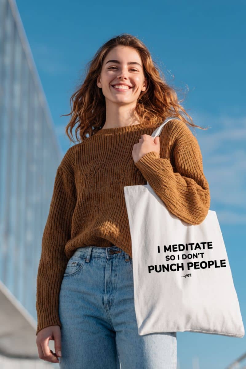 humorous tote bags with a woman holding a tote bag with text 'I Meditate So I Don’t Punch People...yet' against a blue sky