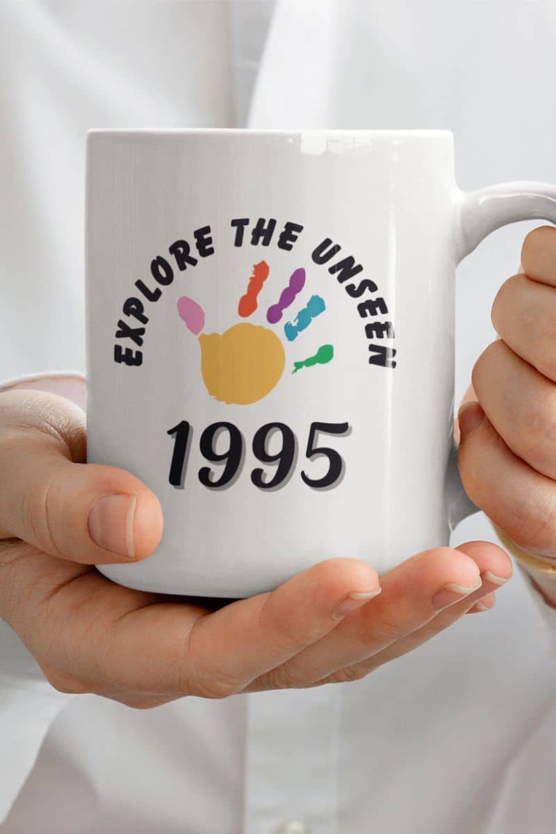 inspirational travel mug with a white mug with 'Explore the Unseen 1995' design held by a person