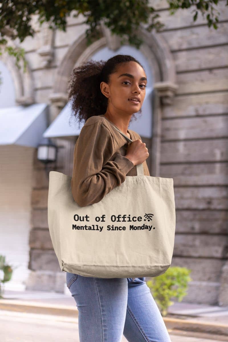 Introvert office tote bag with 'Out of Office. Mentally Since Monday,' carried by a woman in an urban setting.