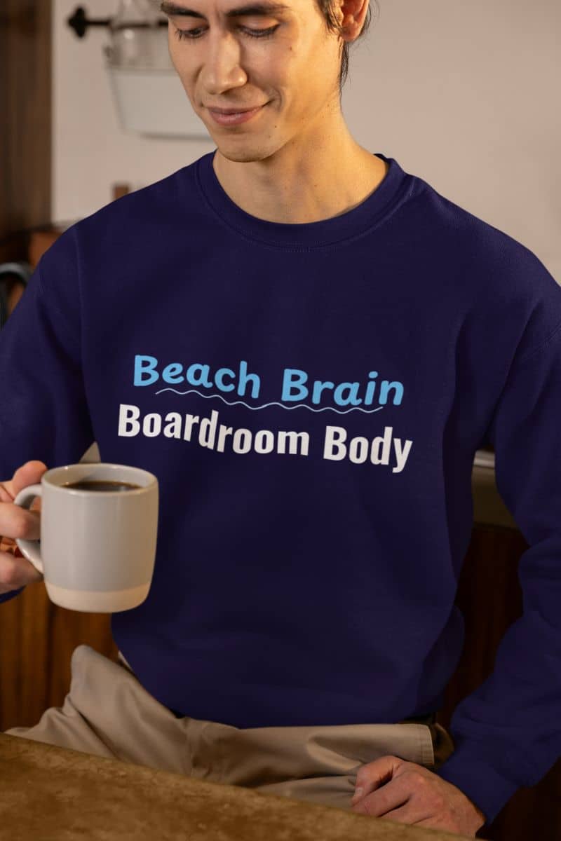 lazy day cozy hoodie with a person wearing a navy blue sweatshirt with 'Beach Brain Boardroom Body' text, holding a mug.