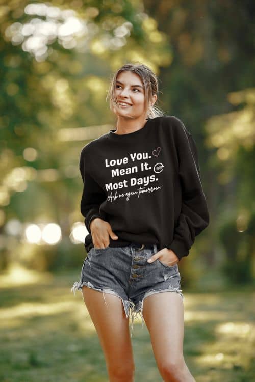 love sarcasm sweatshirt with a woman wearing a black sweatshirt with text 'Love You. Mean It. Most Days. Ask me again tomorrow.' in a forest setting