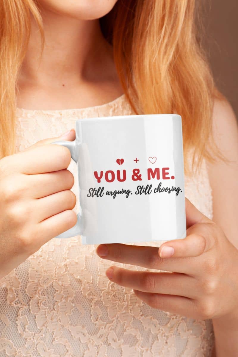 marriage humor mug with a person holding a white mug with text 'YOU & ME. Still arguing. Still choosing.'