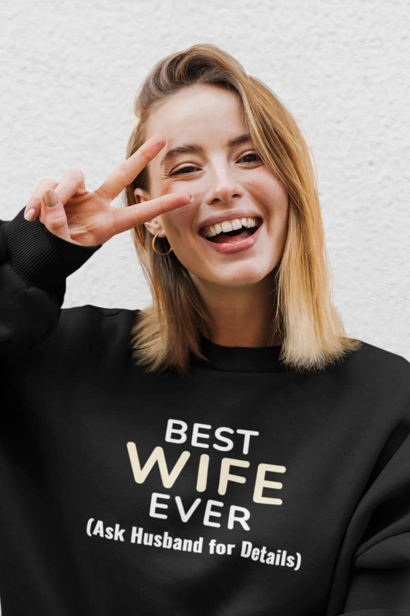 matching couple sweatshirt with a woman wearing a black sweatshirt with 'Best Wife Ever. (Ask Husband for Details)' text, making a peace sign.