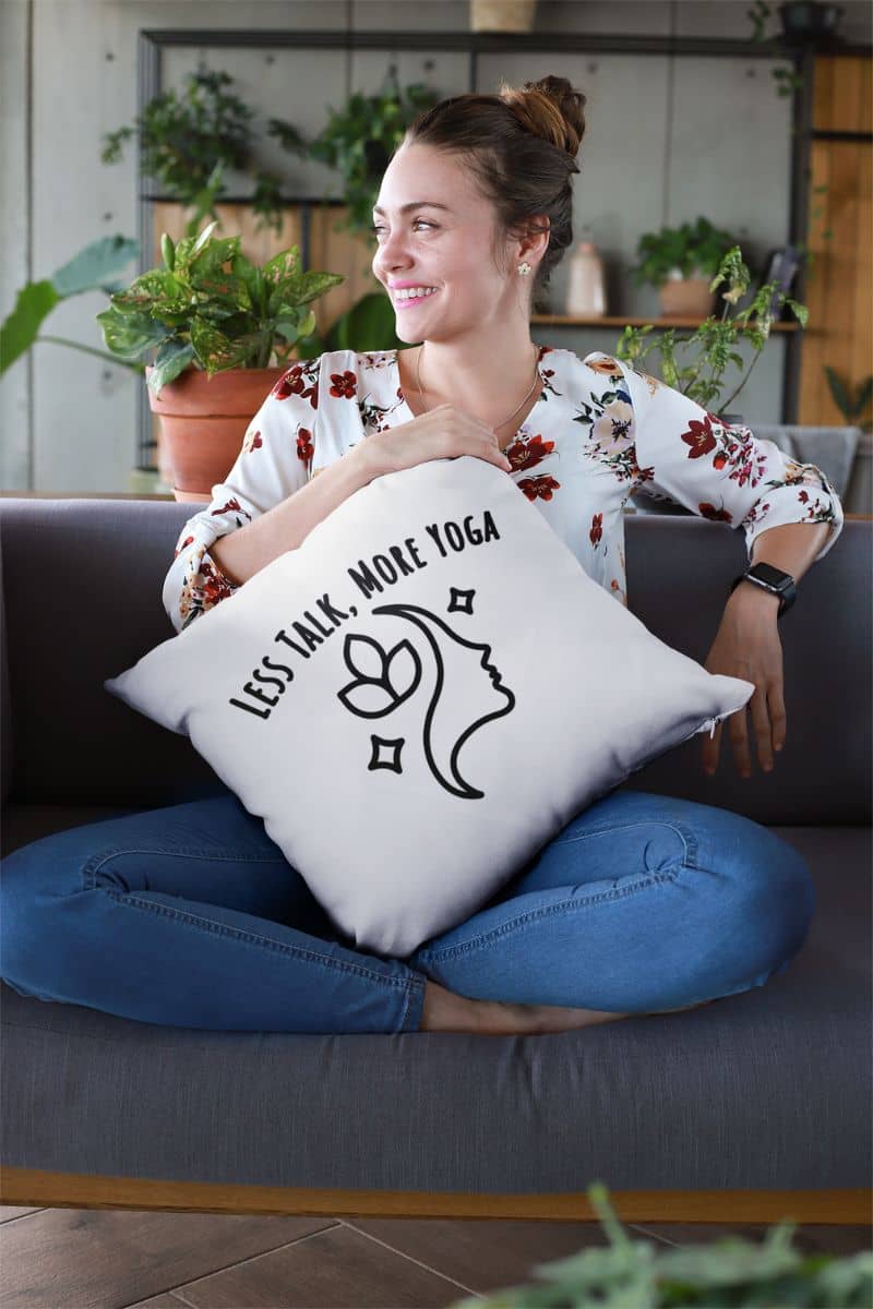 meditation home decor with a woman holding a pillow with text 'Less Talk, More Yoga' , sitting on a couch in a home setting.