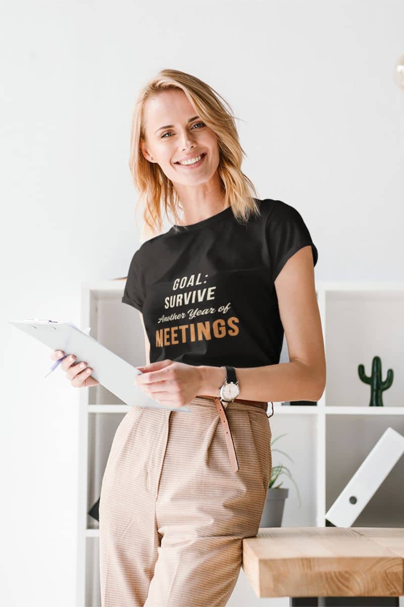 meeting humor tee with a woman wearing a black t-shirt with humorous text, holding a tablet in an office setting.