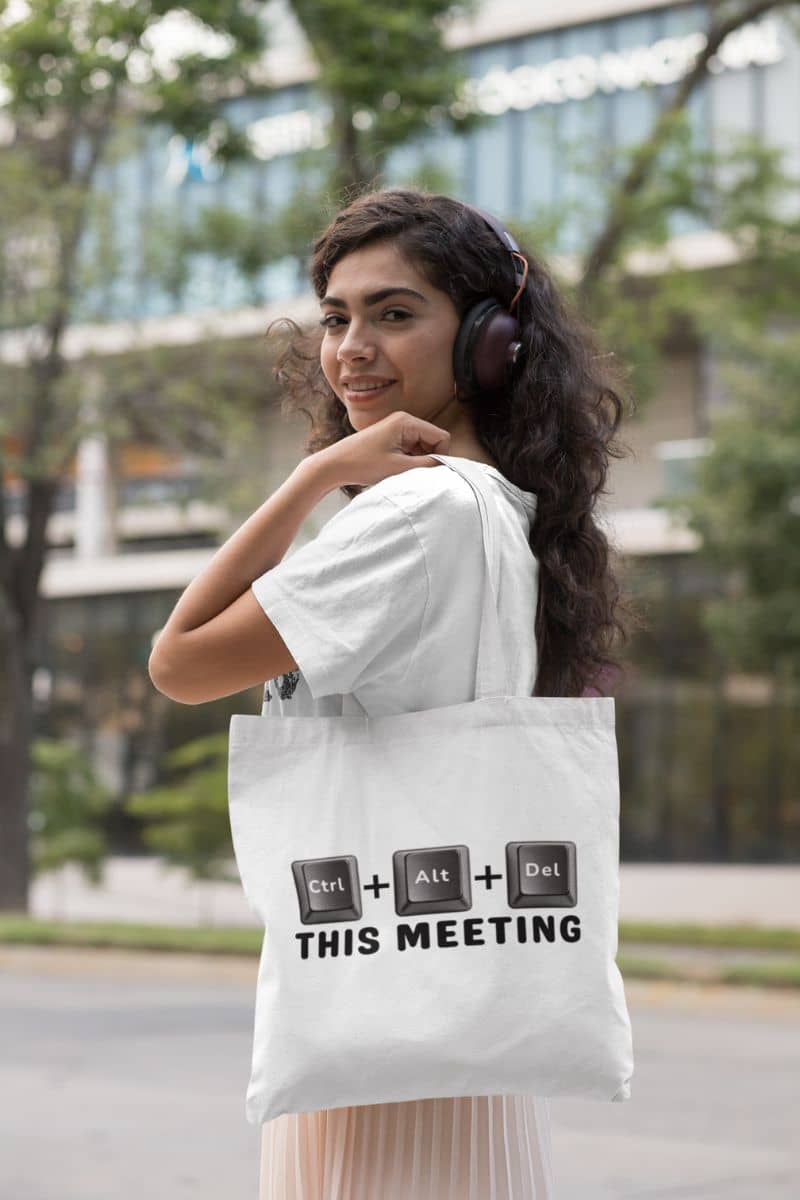 meeting humor tote with a woman wearing headphones and holding a tote bag with text 'Ctrl + Alt + Del This Meeting' in an urban setting