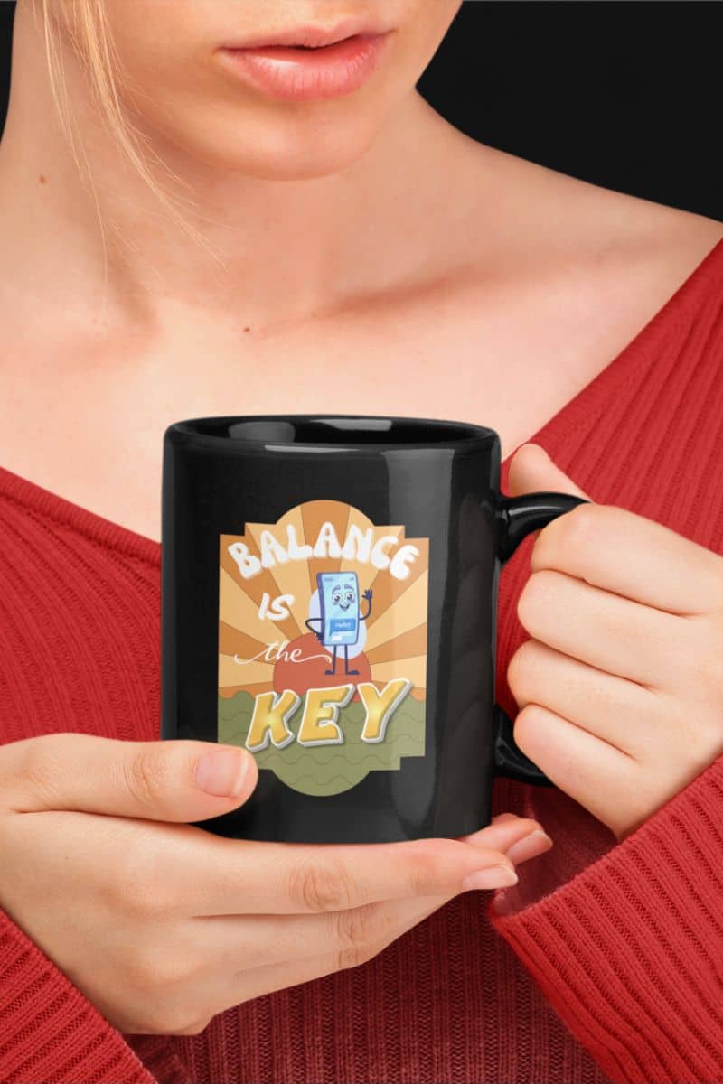 mental balance mug with a person holding a black mug with 'Balance is the Key' design, wearing a red top.