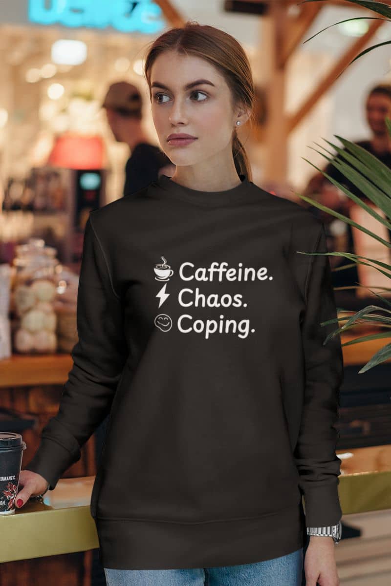 mental health pullover with a woman wearing a black sweatshirt with text 'Caffeine, Chaos & Coping' in a casual setting