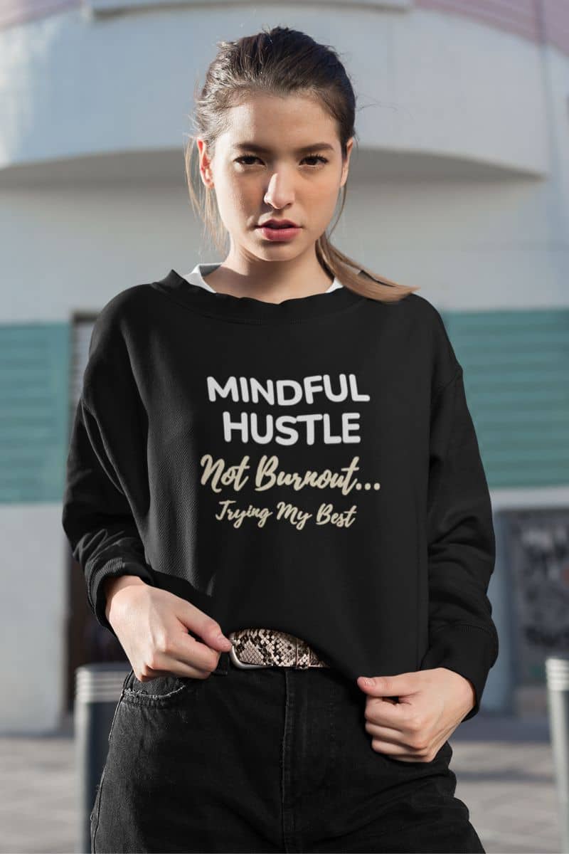 mental health sweatshirt with a woman wearing a black sweatshirt with motivational text 'Mindful Hustle – Not Burnout… Trying My Best', standing outdoors.