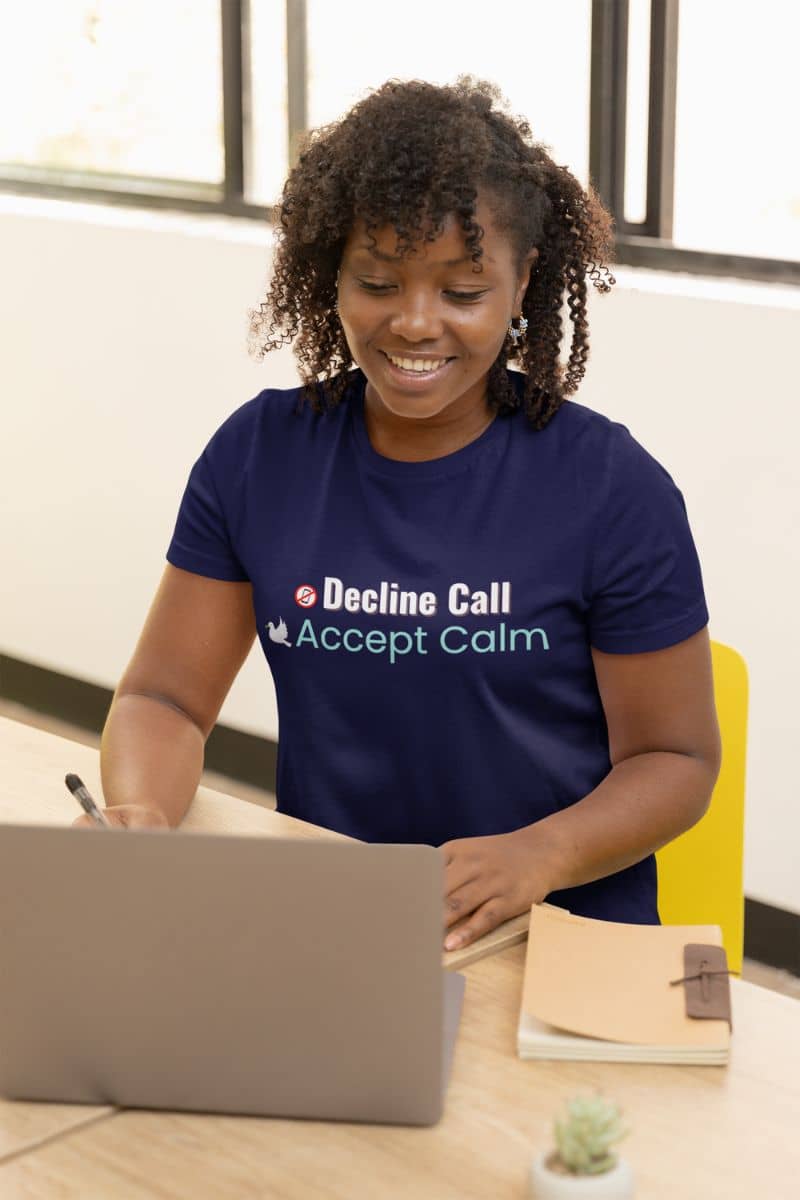 mindful quote shirt with a person wearing a blue t-shirt with text 'Decline Call, Accept Calm', sitting at a desk with a laptop.