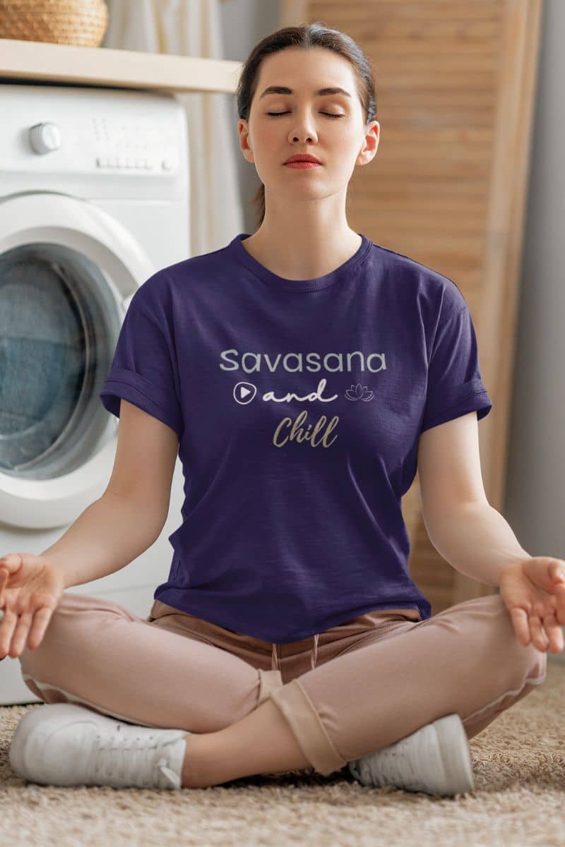 mindful yoga shirt with a person wearing a purple t-shirt with 'Savasana and Chill' text, sitting in a meditative pose in a home setting.