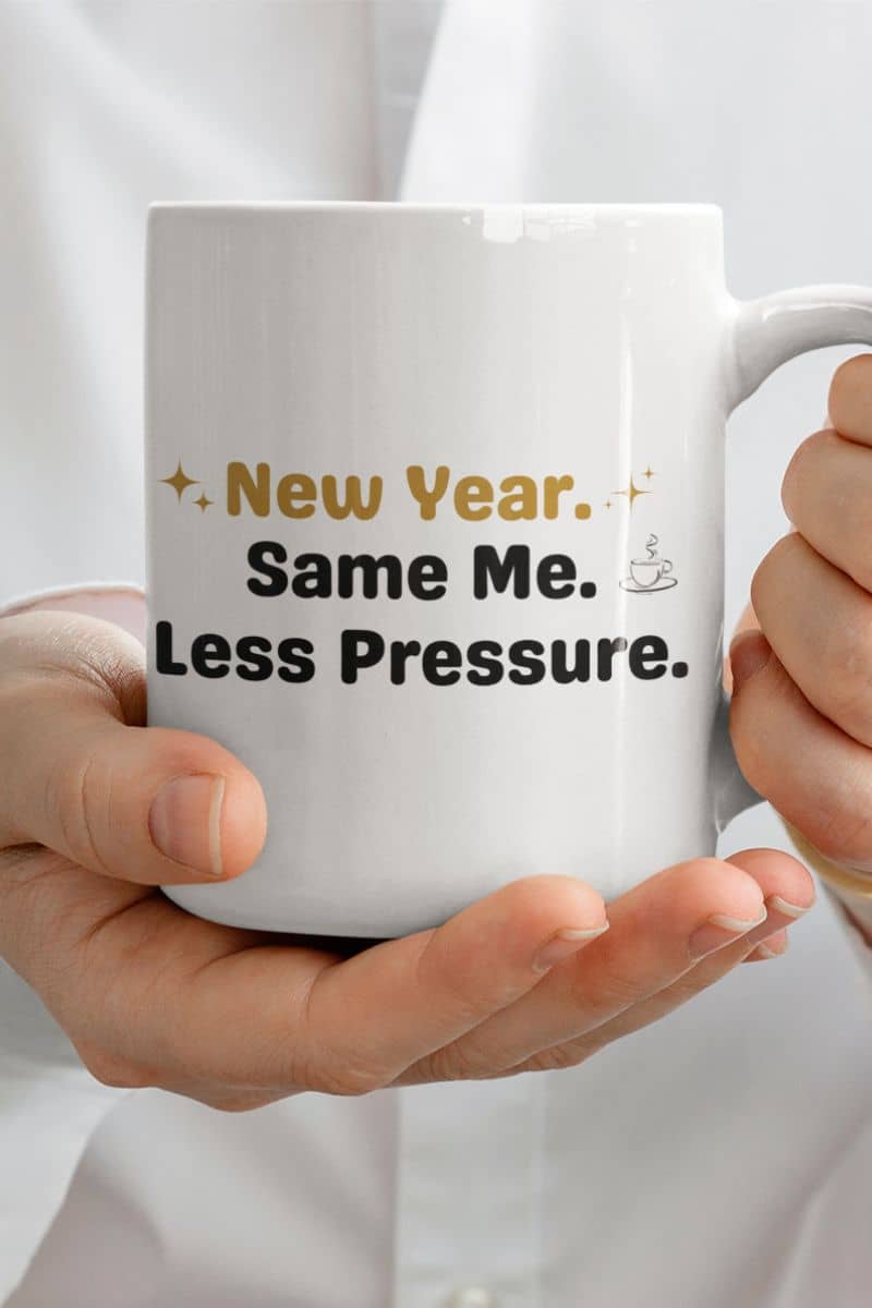 mindfulness coffee mug with a white mug with text 'New Year. Same Me. Less Pressure.' held by a person, against a plain background