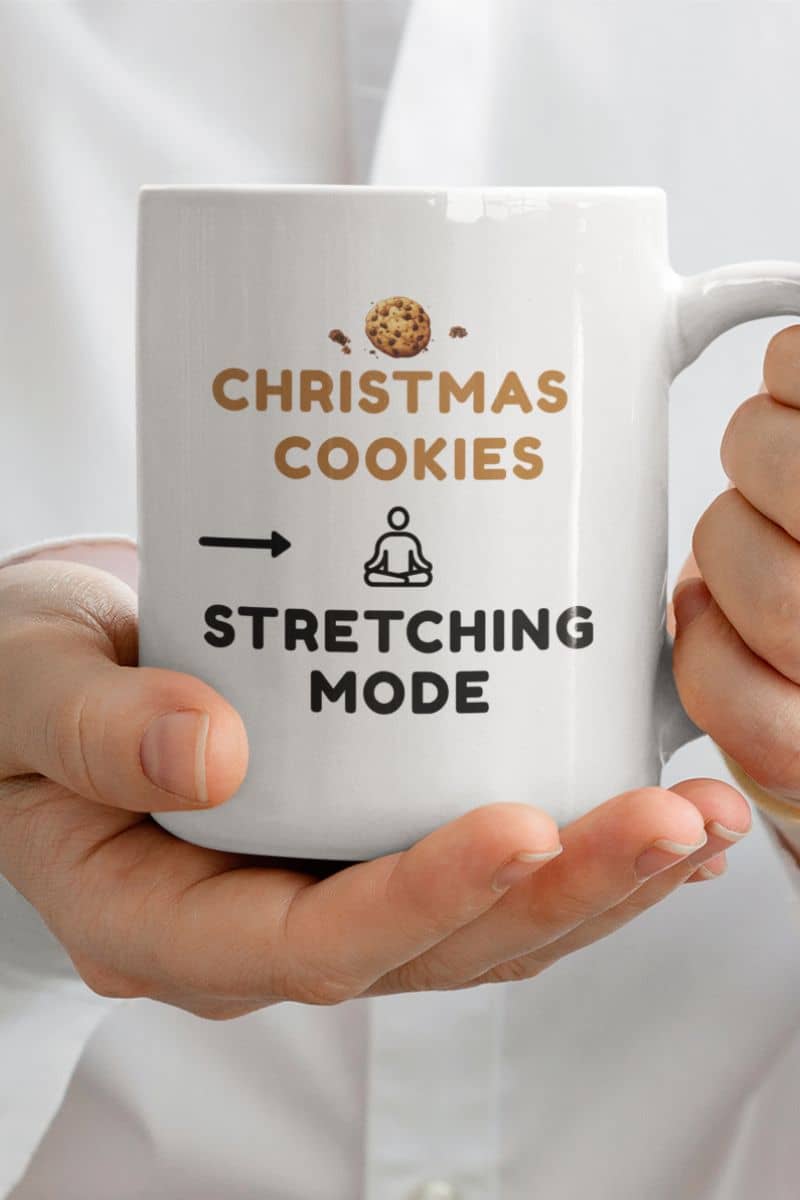 mindfulness holiday coffee mug with a white mug with text 'Christmas Cookies, Stretching Mode' held by a person.