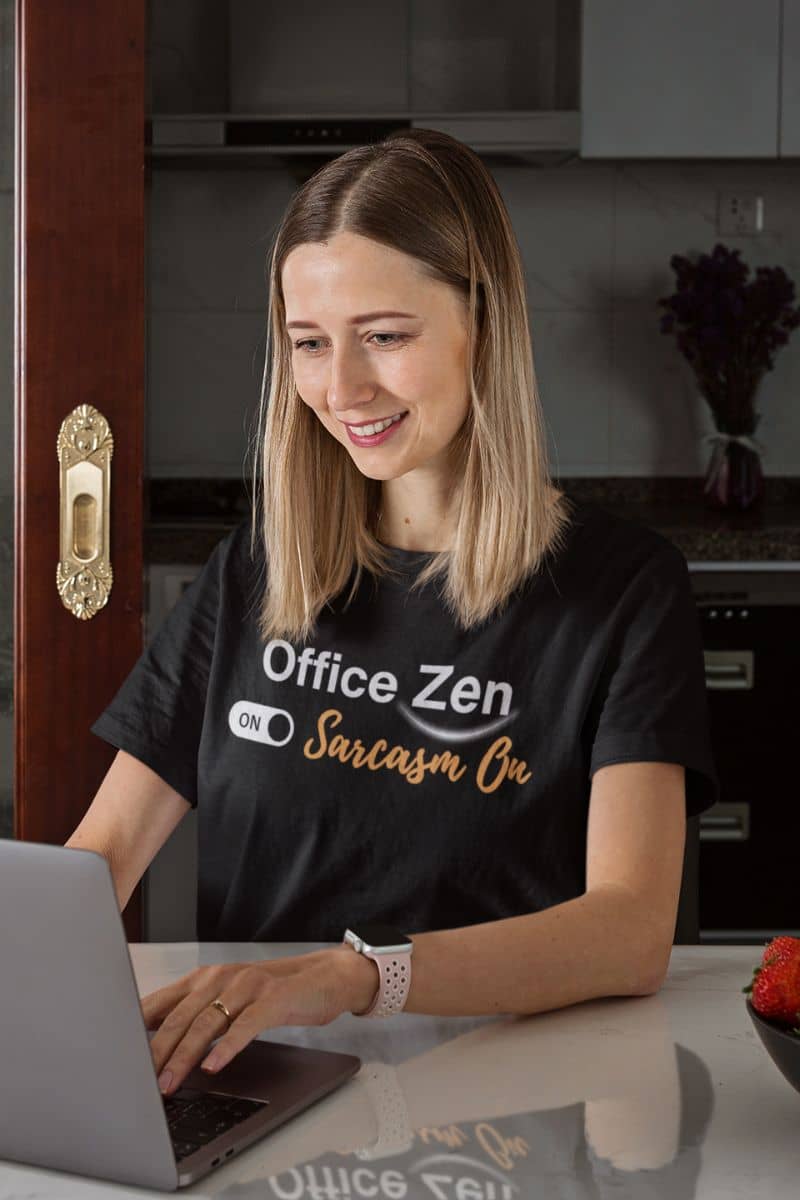 mindfulness humor tee with a woman wearing a black 'Office Zen on Sarcasm On' t-shirt using a laptop in a kitchen.