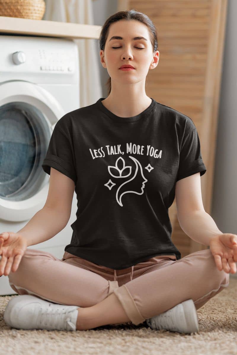 mindfulness quote tee with a woman meditating in a room with a washing machine, wearing a black t-shirt with 'LESS TALK, MORE YOGA' text.