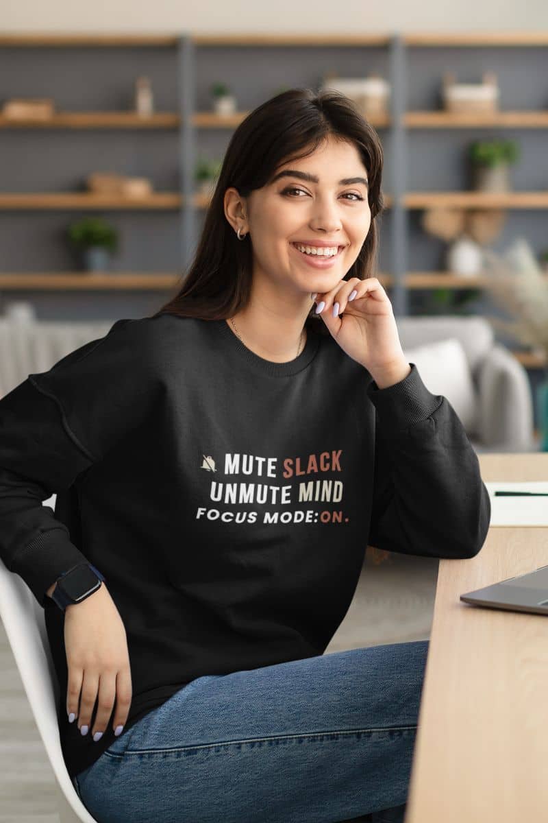 mindfulness sweatshirt with a woman wearing a black sweatshirt with text 'Mute Slack, Unmute Mind. Focus Mode: On', sitting in an office setting.