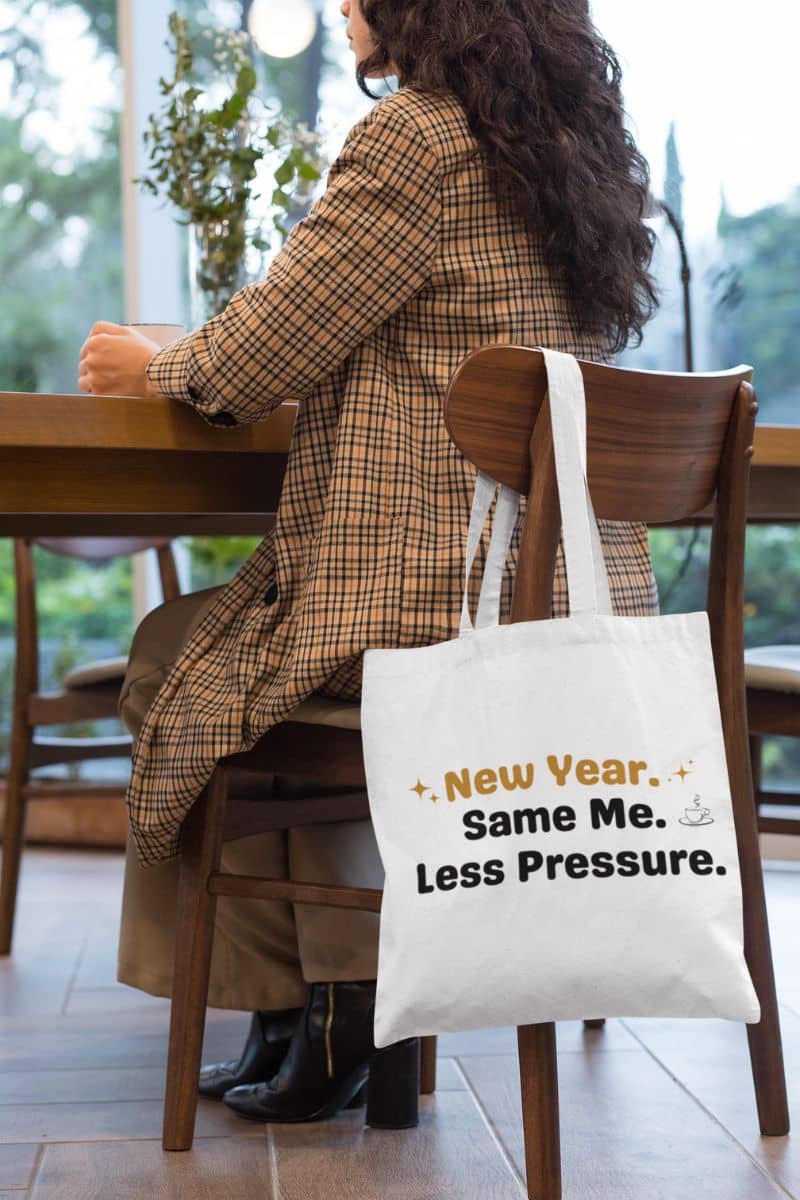 minimalist canvas tote with a person sitting at a table with a tote bag featuring text 'New Year. Same Me. Less Pressure.'.