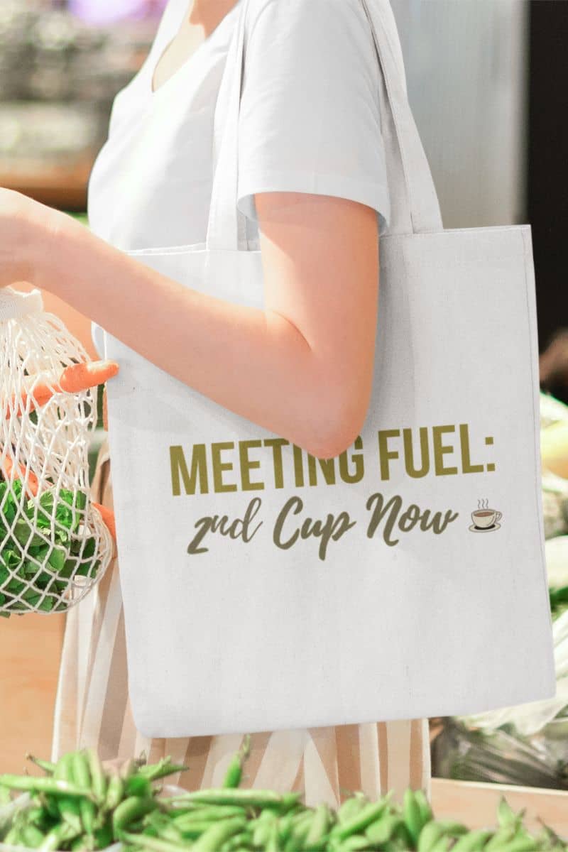 minimalist coffee tote with a person holding a tote bag with humorous text design, surrounded by greenery.