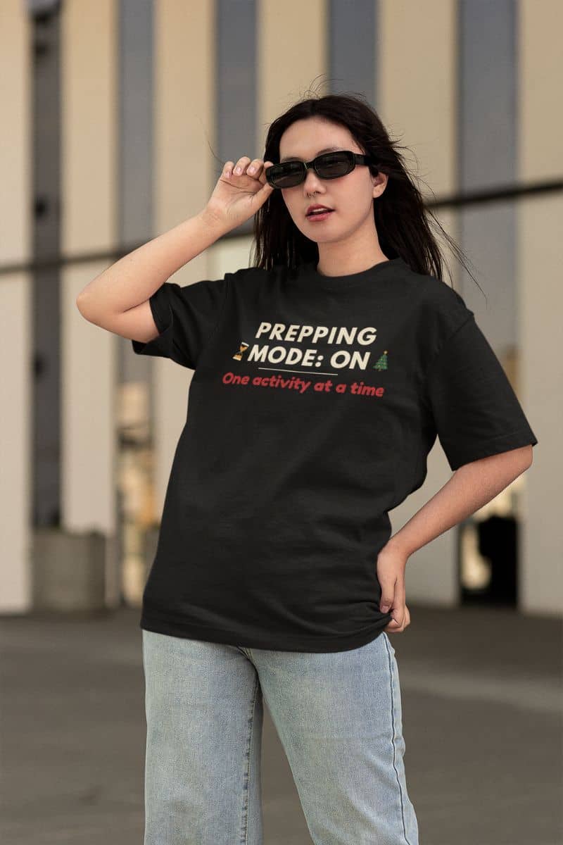 minimalist holiday shirt with a person wearing a black t-shirt with text 'Prepping Mode: ON – One activity at a time', standing outdoors.