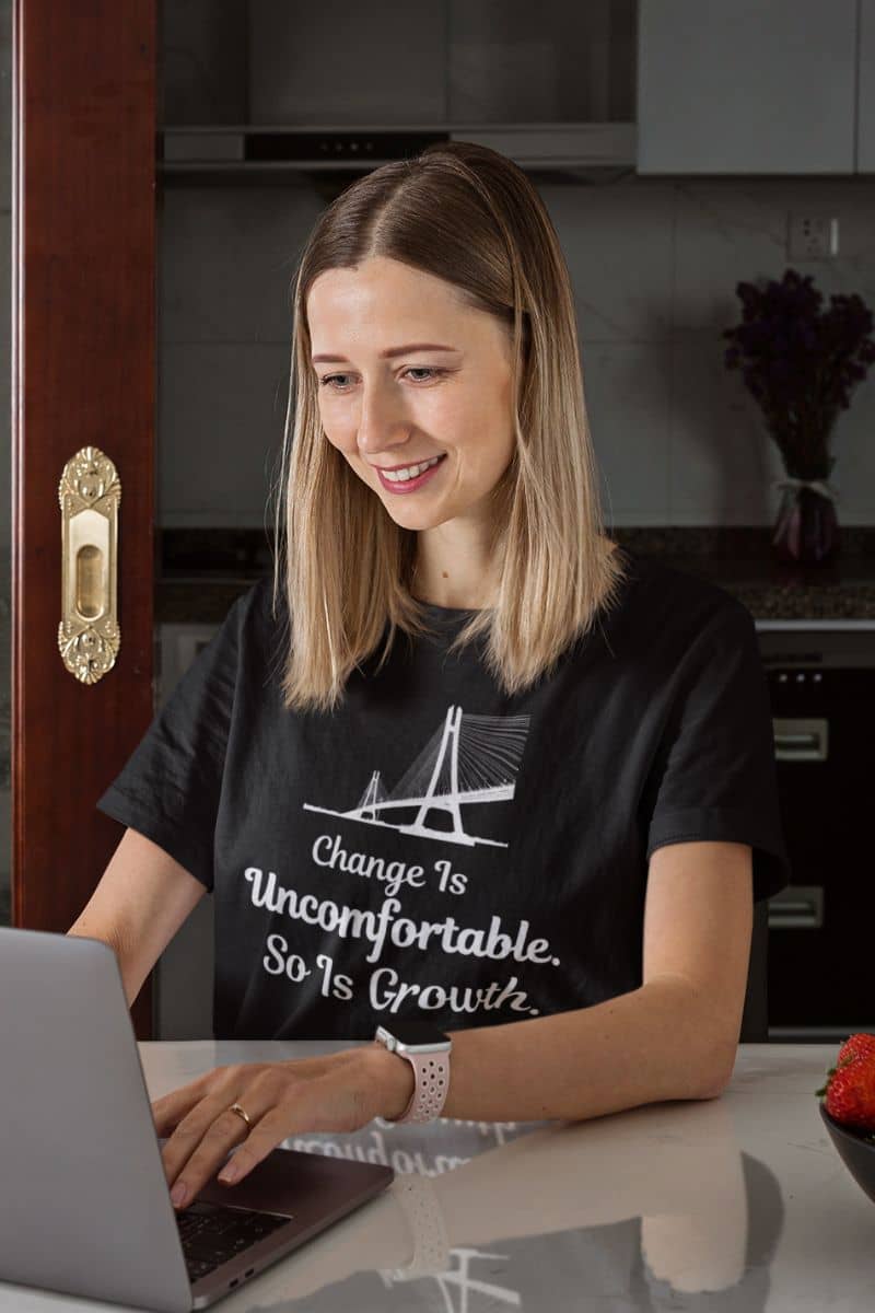 minimalist quote t-shirt with a woman wearing a black t-shirt with a motivational quote, sitting at a table with a laptop.