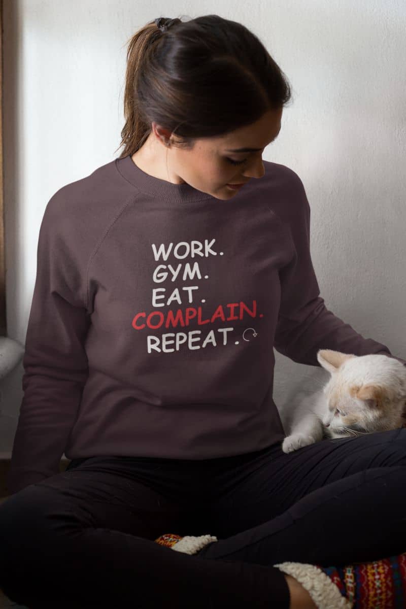 minimalist sweatshirt with a person in a sweatshirt with text 'Work. Gym. Eat. Complain. Repeat', sitting next to a cat.