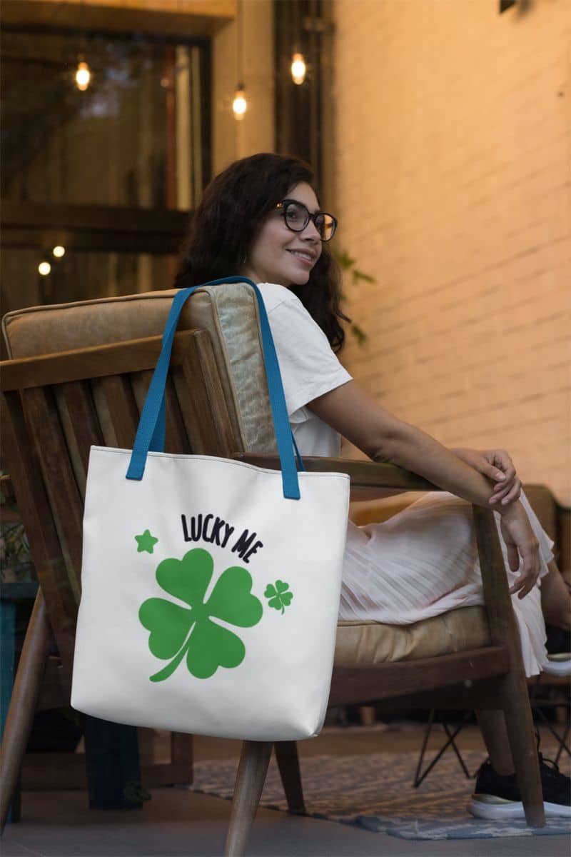 minimalist tote bag with a woman sitting on a chair holding a tote bag with a four-leaf clover design and 'Lucky Me' text.