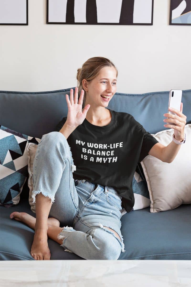 minimalist work humor tee with a woman sitting on a couch wearing a black t-shirt with text, using a phone.