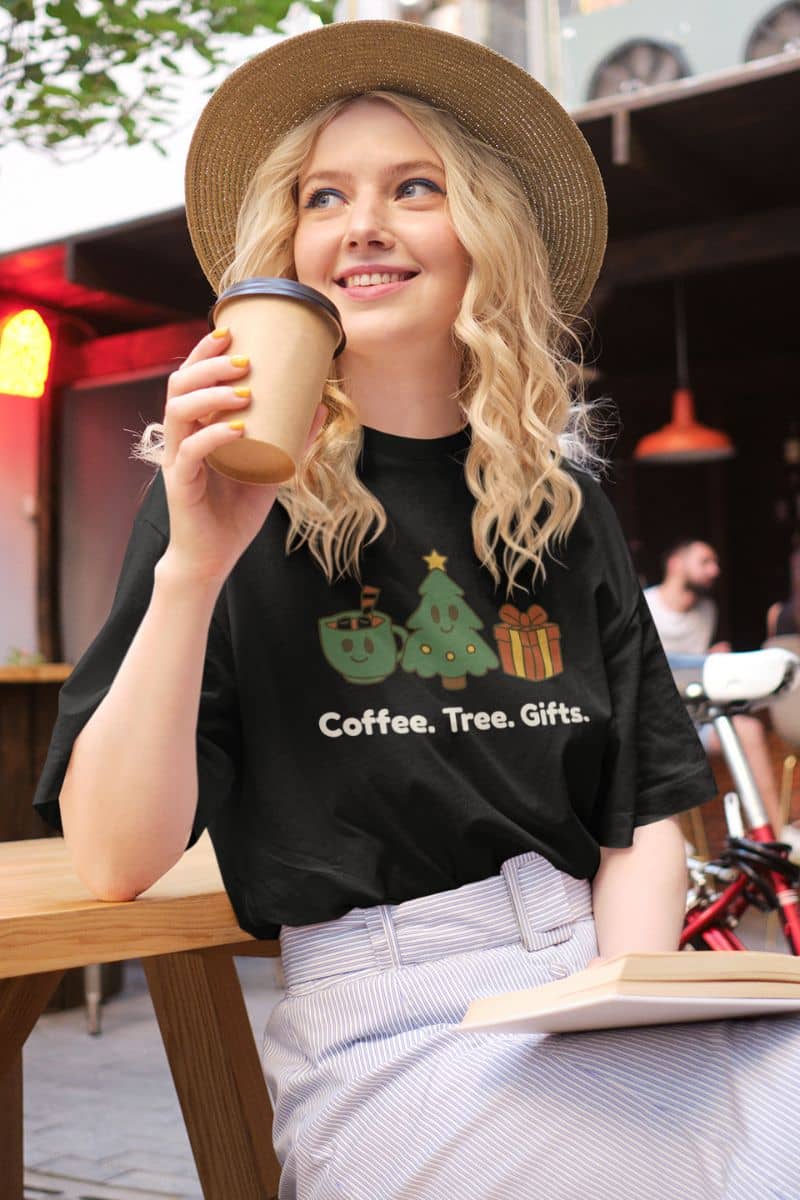 modern christmas shirt with a woman wearing a black t-shirt with a Christmas-themed design, holding a coffee cup outdoors.