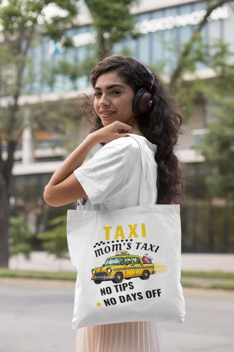 mom driver tote bag with a woman holding a tote bag featuring the text 'Taxi, Mom’s Taxi – No tips, no days off' in an urban setting