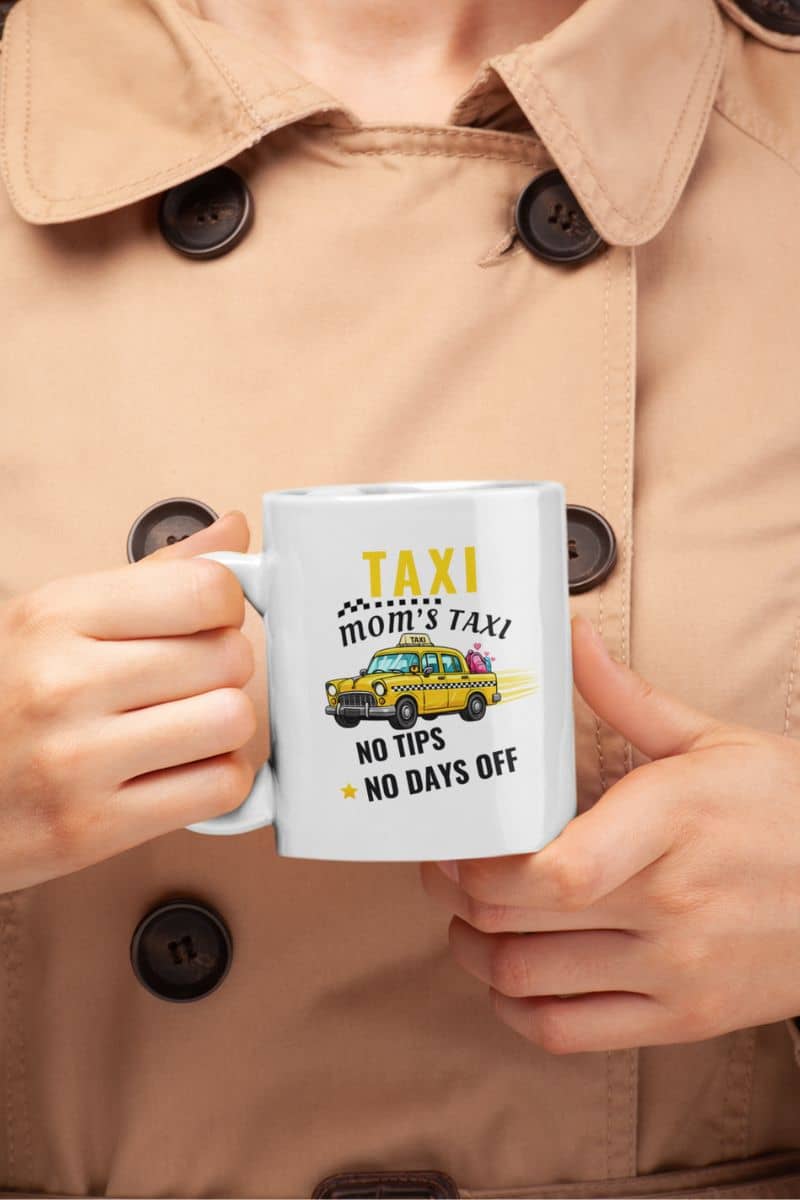 mom taxi mug with a person holding a mug with a taxi-themed design and text 'Taxi, Mom’s Taxi – No tips, no days off', wearing a beige coat.