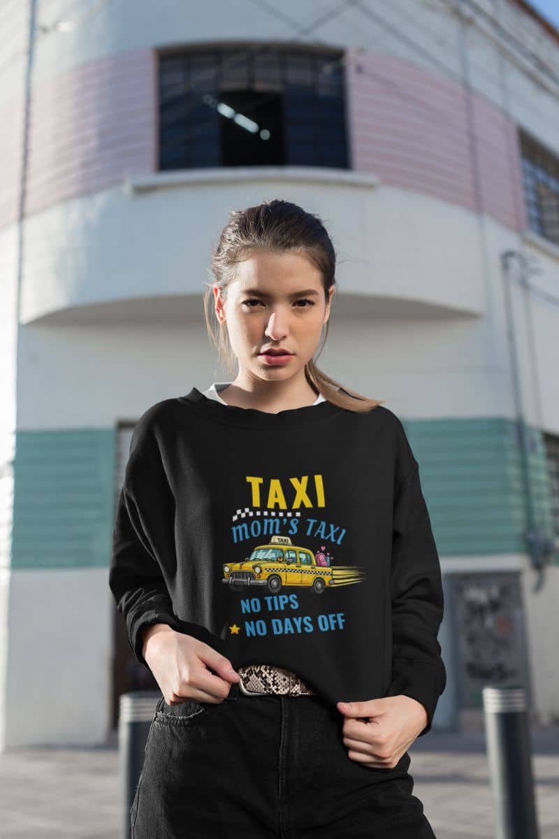 mom taxi sweatshirt with a woman wearing a black sweatshirt with a graphic design in front of a building.