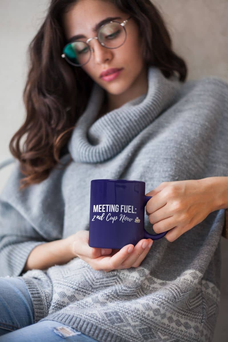 morning motivation mug with a woman holding a blue mug with text 'Meeting Fuel: 2nd Cup Now', wearing a gray sweater.