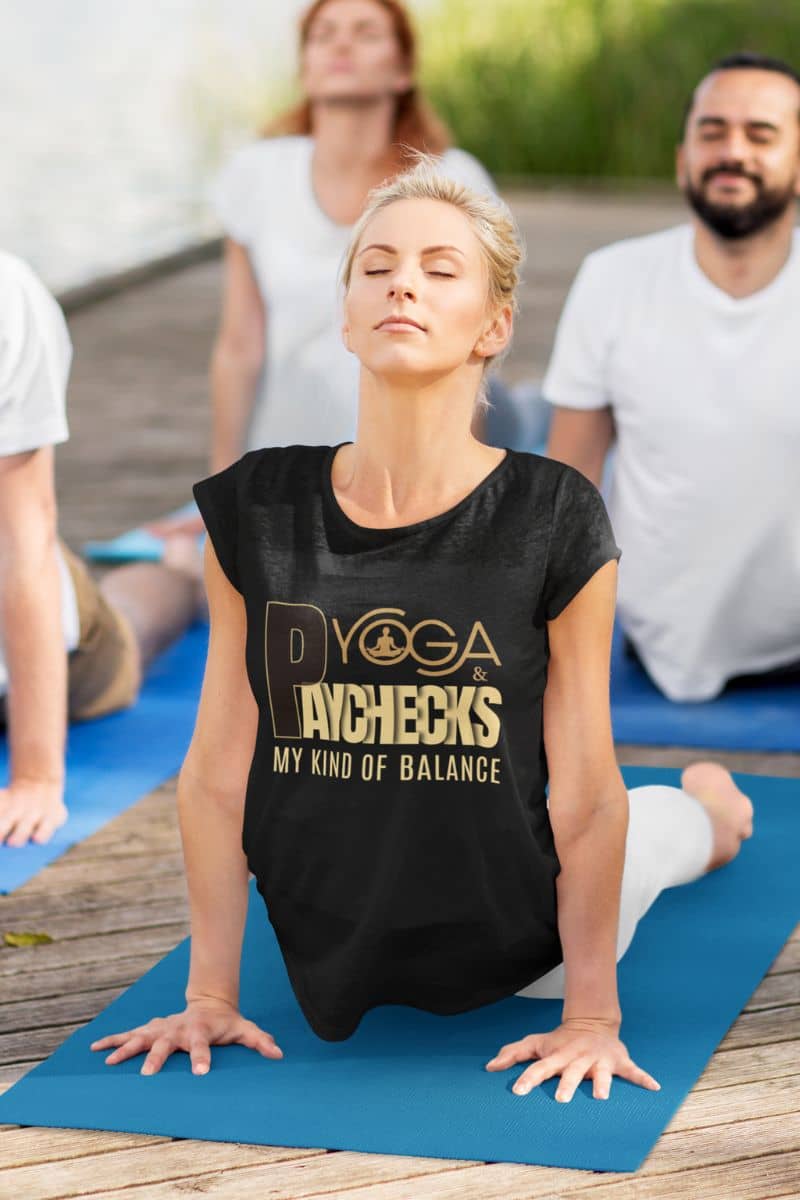 motivational quote shirt with a woman in a black t-shirt with yoga-themed text on a blue mat, surrounded by others in a yoga class.