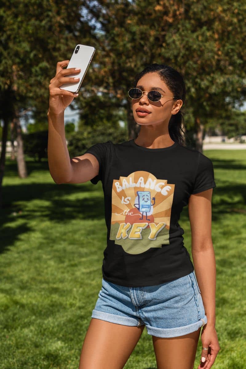 motivational shirt for her with a woman taking a selfie outdoors wearing a black t-shirt with 'Balance is the Key' design.