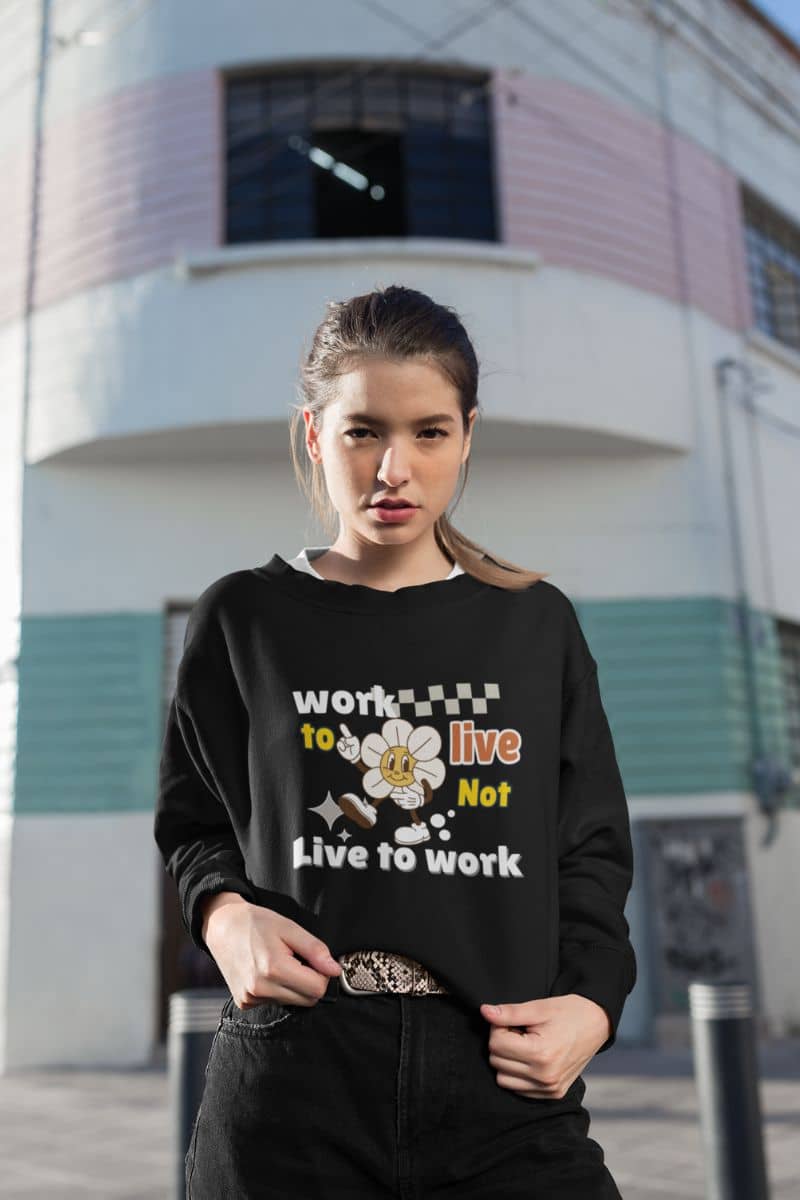motivational sweatshirt with a woman wearing a black sweatshirt with text 'Work to Live, Not Live to Work' in front of a building.
