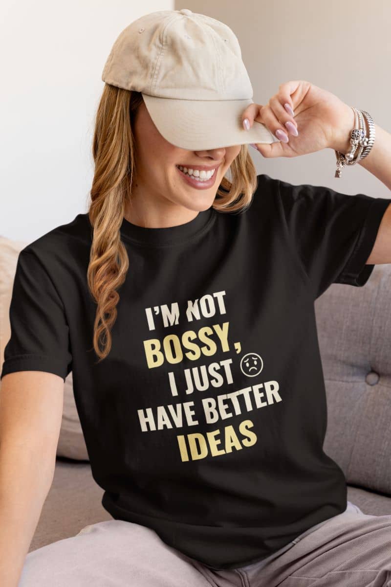 motivational work quote shirt with a person wearing a black t-shirt with text 'I’m Not Bossy, I Just Have Better Ideas', sitting on a couch.