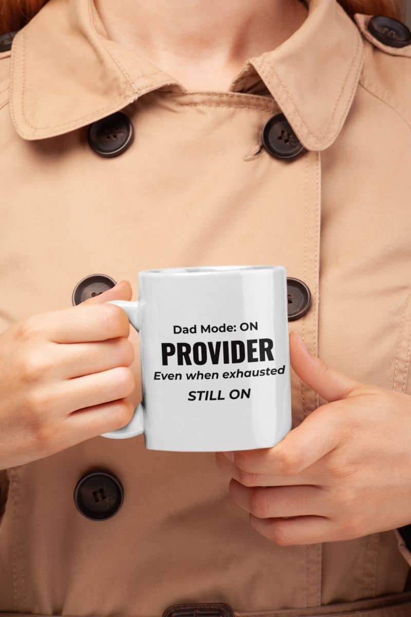 mug for dad with a person holding a mug featuring the text “Dad Mode: On. Provider. Even when exhausted. Still on” against a beige coat background