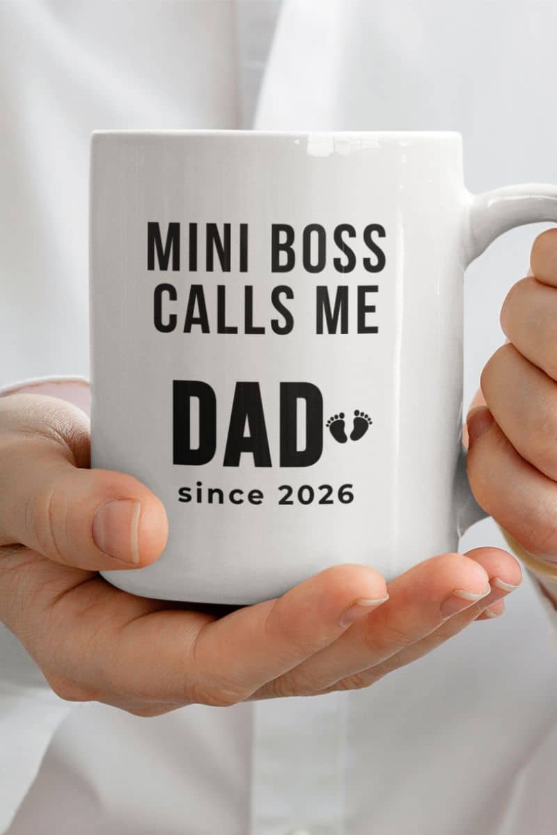 new dad gift mug with a white mug with text 'MINI BOSS CALLS ME DAD since 2026' held by hands against a light background
