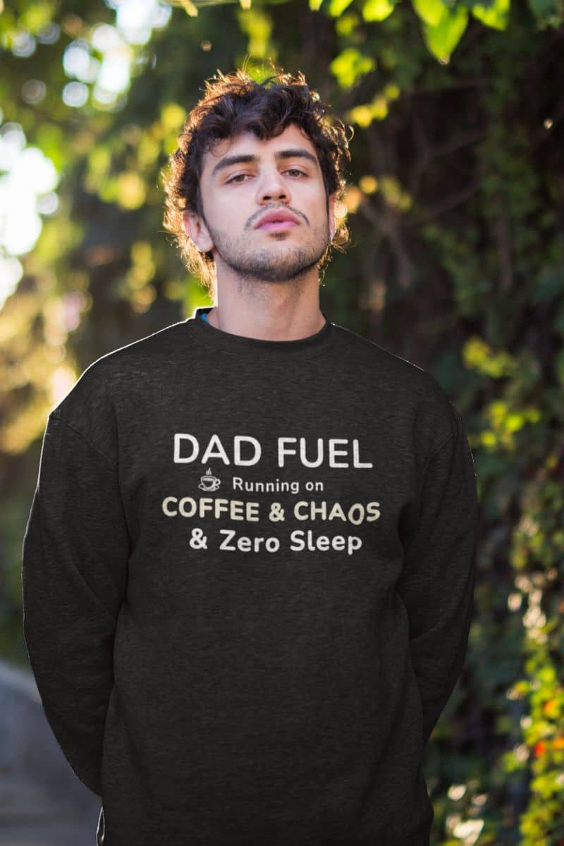 new dad humor sweatshirt with a man wearing a black sweatshirt with text 'DAD FUEL – Running on Coffee & Chaos & Zero Sleep' in an outdoor setting
