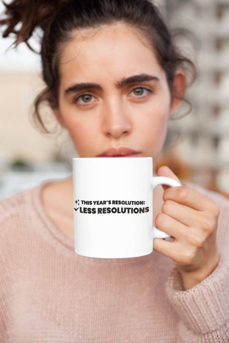 new year resolution mug with a woman holding a mug with text 'This year’s resolution: Less resolutions.' against a blurred background