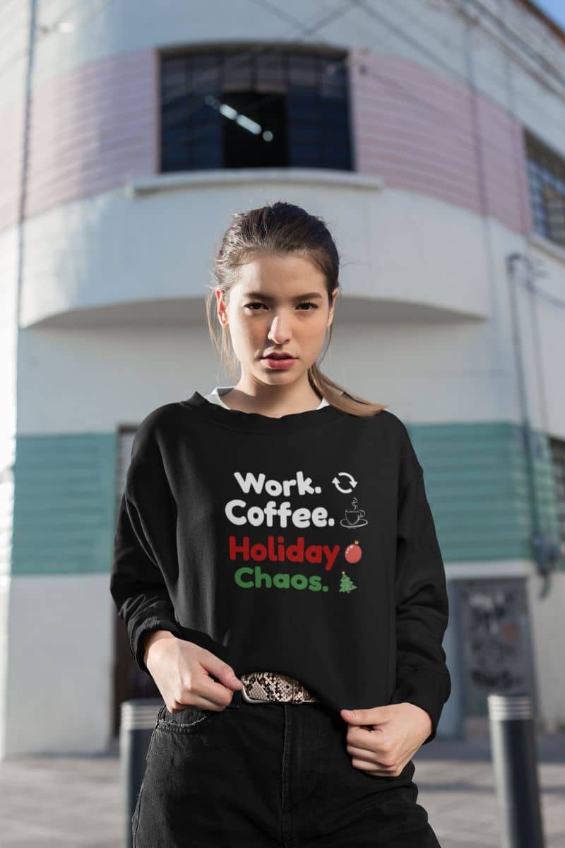 office burnout sweater with a woman wearing a black sweatshirt with text 'Work. Coffee. Holiday Chaos.' in an urban setting