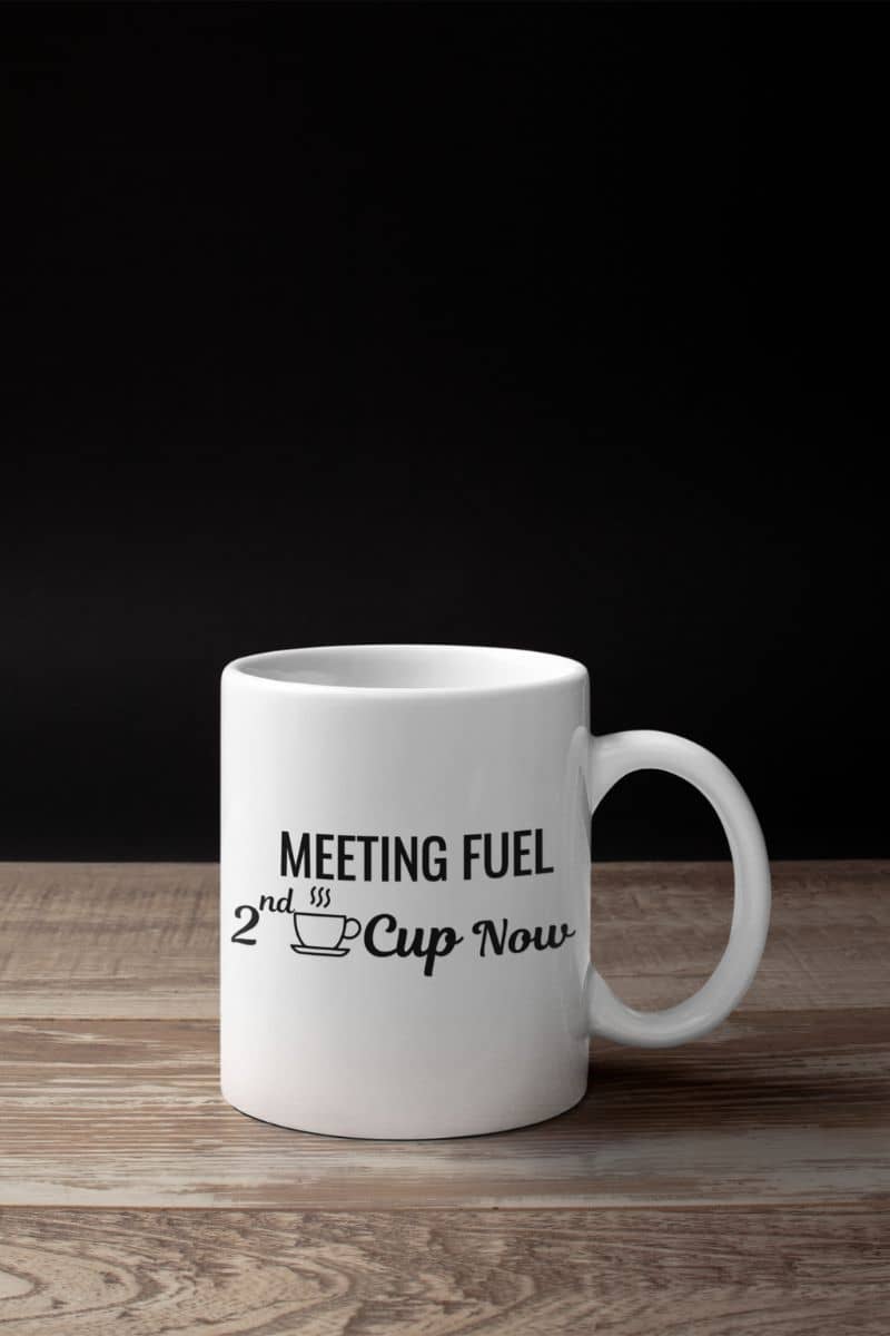 office desk mug with a white mug with text 'Meeting Fuel: 2nd Cup Now' on a wooden surface and black background
