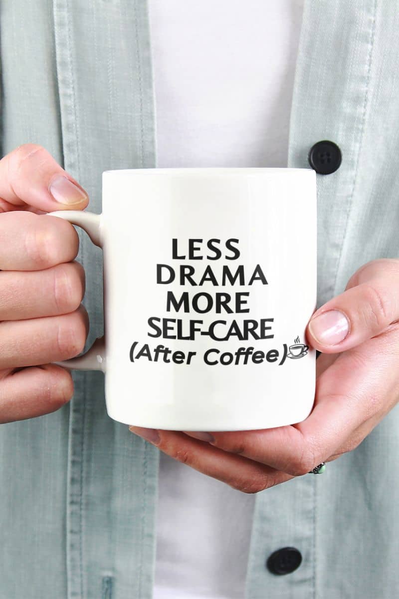office humor mug with a person holding a mug with 'Less Drama, More Self-Care (After Coffee)' text.